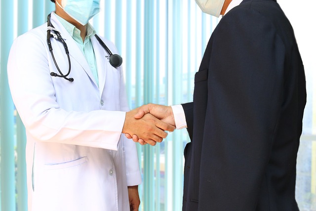 Male physician wearing a white lab coat and stethoscope shaking hands with a patient in a dark suit at Riverside Cardiology Associates.